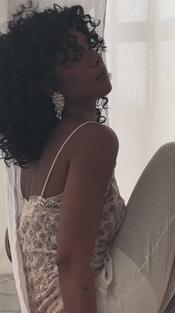 Woman wearing pearl statement earrings near a window.